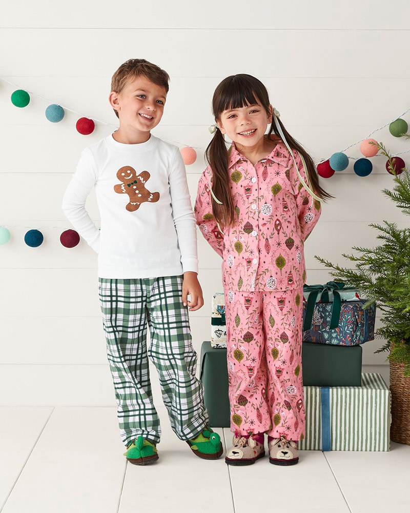 A boy and girl wearing holiday pajamas with cute animal slippers. Browse the Kids' Shop.