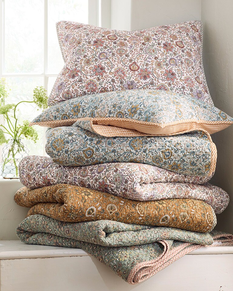 A stack of our Odette Floral Organic-Cotton Voile quilts and shams in various colors. Shop quilts.