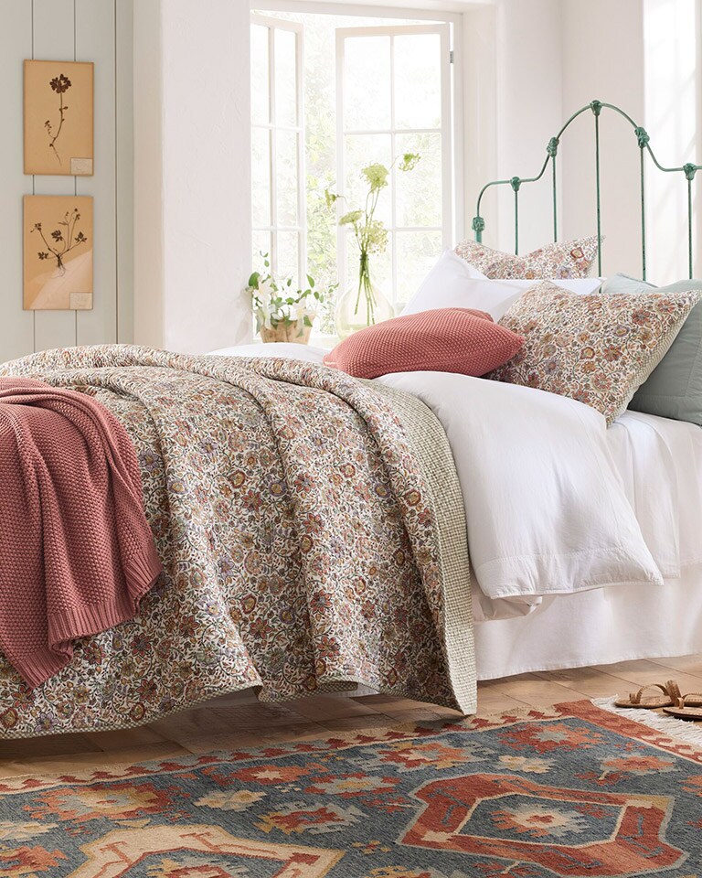 A bed with colorful summer bedding and our Odette Floral Organic-Cotton Voile quilt. Shop quilts.