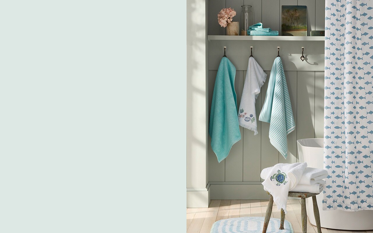 A bathroom with towels, mats, and shower curtains in blues, greens and summer prints. Shop bath.