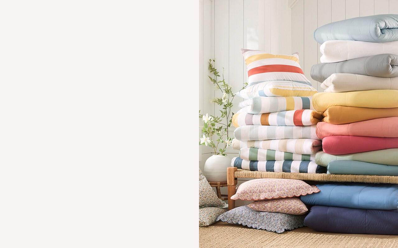 A stack of colorful comforters & pillows. Shop comforters.