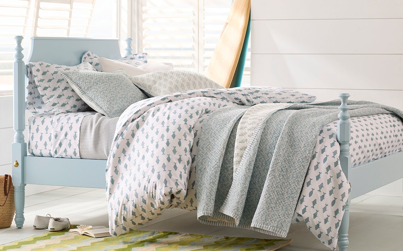 A bed with cotton percale bedding in a turquoise fish print. Shop sheets.
